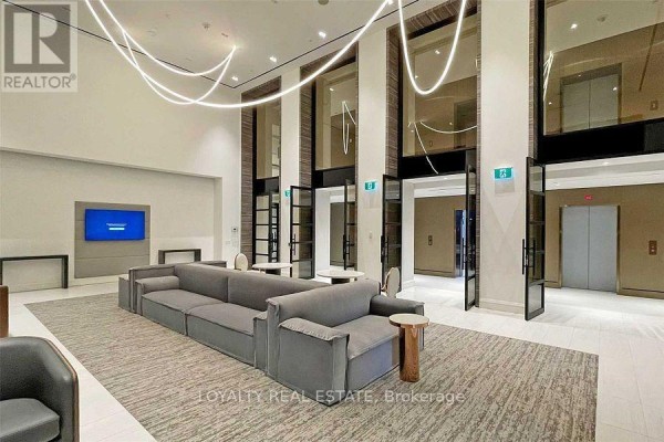 Contemporary building lobby with grey sectional sofa, modern lighting, and elevators. - 1409 - 39 Roehampton Avenue, Toronto