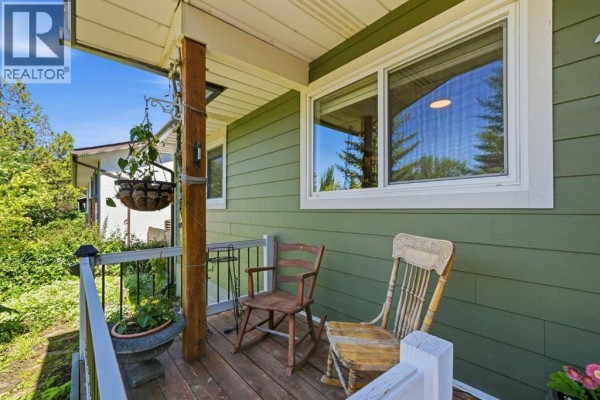 Covered front porch with wood decking, railing, and two rocking chairs. - 1409 Idaho Street, Carstairs