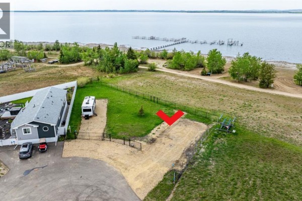 Sandy beach shoreline with grass and trees, overlooking a calm body of water on a clear day. - 141, 41310 Range Road 282, Rural Lacombe County