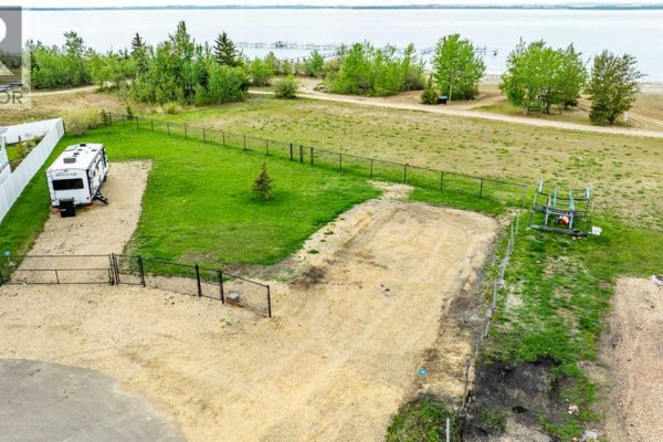 View of a lake through a chain-link fence, with bare trees and a small evergreen on a sunny day. - 141, 41310 Range Road 282, Rural Lacombe County