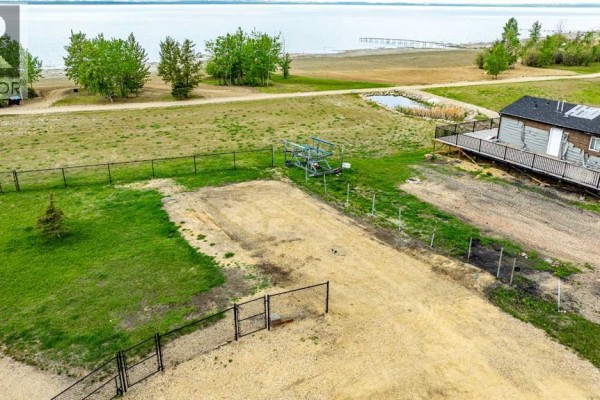 Chain-link fence bordering an undeveloped lot with tire tracks, trees, and a view of a distant lake. - 141, 41310 Range Road 282, Rural Lacombe County