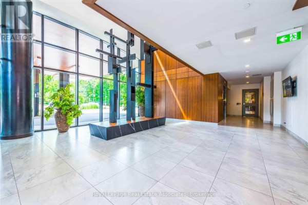 Apartment building lobby with marble floors, large windows, wood paneling, and modern sculpture. - 141 - 1575 Lakeshore Road W, Mississauga