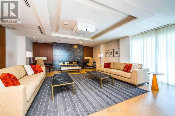 Apartment building lounge with two sofas, fireplace, coffee tables, and large windows. - 141 - 1575 Lakeshore Road W, Mississauga