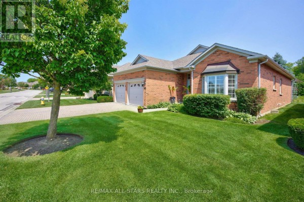 Side view of a brick house with two garage doors, a manicured lawn, and a large tree. - 141 - 86 Legendary Trail, Whitchurch Stouffville