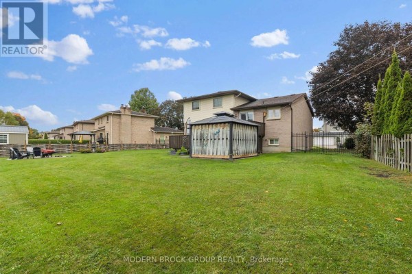 Backyard of a residential property with a grassy lawn, wooden deck, and covered gazebo. - 141 Beley Street, Brockville
