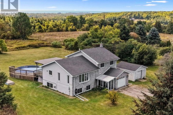 Rear aerial view of a two-story house with a wooden deck and round swimming pool, next to a detached garage. - 141 Cedar Lane, Cramahe