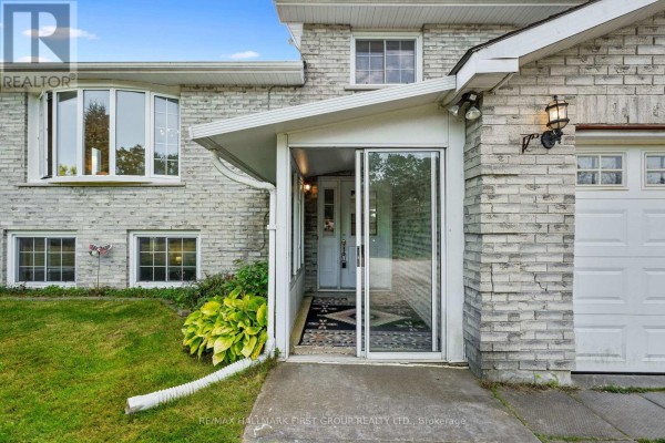 Close-up of the covered entryway of a grey brick house, featuring a sliding glass door and welcome mat. - 141 Cedar Lane, Cramahe