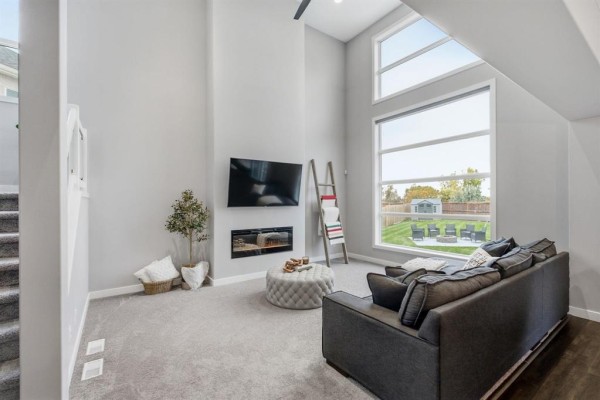 Living room with a fireplace, grey sofa, tufted ottoman, and floor-to-ceiling windows. - 141 Daylan Marshall Gate, Winnipeg