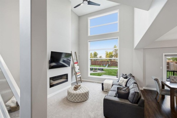 Living room with a large sofa, fireplace, and tall windows overlooking the backyard. - 141 Daylan Marshall Gate, Winnipeg