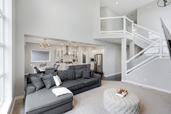 Open-concept living space with grey sectional sofa, kitchen, and modern staircase. - 141 Daylan Marshall Gate, Winnipeg