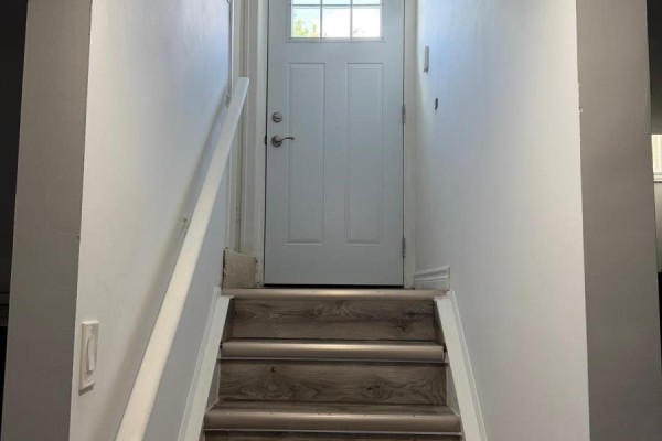Interior view of a narrow staircase leading up to a white front door with a glass pane. - 141 Gail Parks Crescent, Newmarket