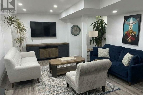 A furnished basement living room with a navy sofa, two armchairs, a coffee table, and a television. - 141 Gail Parks Crescent, Newmarket
