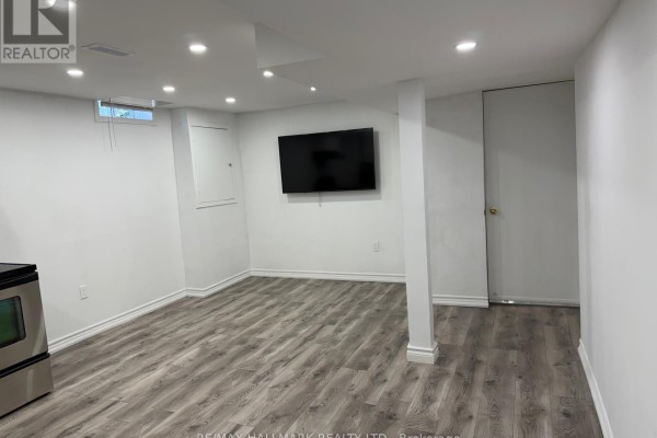 An unfurnished basement room with white walls, a television mounted on the wall, and grey laminate flooring. - 141 Gail Parks Crescent, Newmarket
