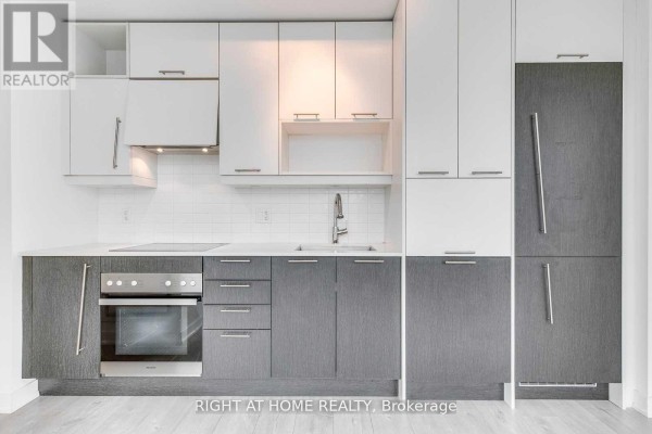 Kitchen with grey and white two-tone cabinets, stainless steel appliances, and white tiled backsplash. - 1410 - 199 Richmond Street W, Toronto