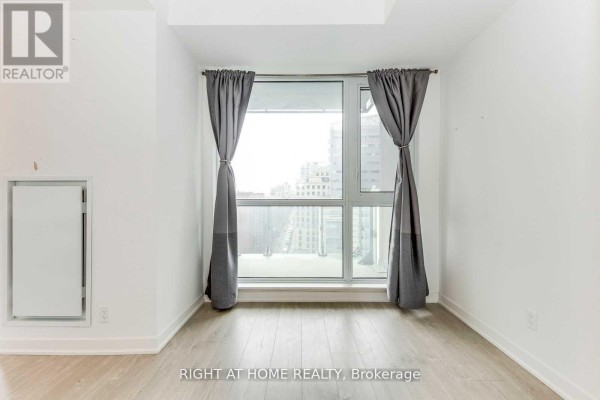Bedroom or living space with large window covered by grey curtains, overlooking the city. - 1410 - 199 Richmond Street W, Toronto