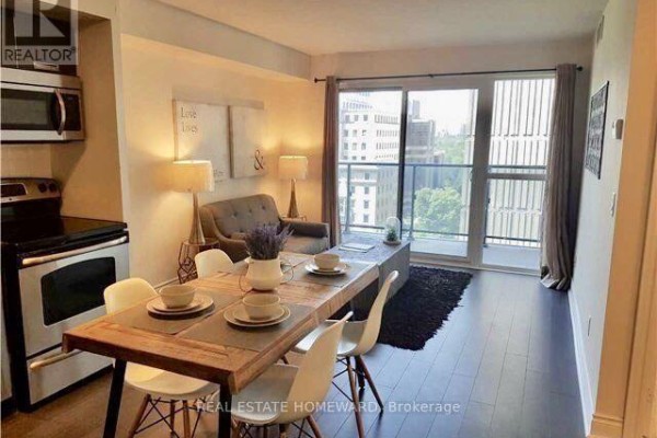 Apartment living and dining area with stainless steel appliances, wooden table, and balcony access. - 1410 - 28 Ted Rogers Way, Toronto