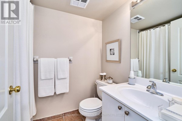 A bathroom with a toilet, vanity with sink, mirror, and shower curtain. - 1411 - 1000 The Esplanade Road N, Pickering