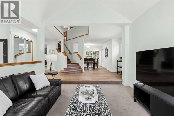 Living room with a black leather sofa, coffee table, and stairs leading to the dining area. - 14125 Evergreen Street Sw, Calgary