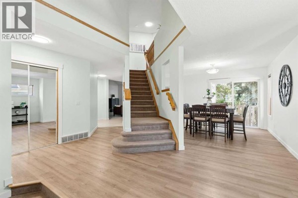 Foyer with carpeted stairs, light wood laminate flooring, and a dining area with a table. - 14125 Evergreen Street Sw, Calgary