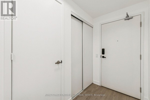 Entryway of the apartment with white walls, closet doors, and a front door. - 1413 - 3900 Confederation Parkway, Mississauga