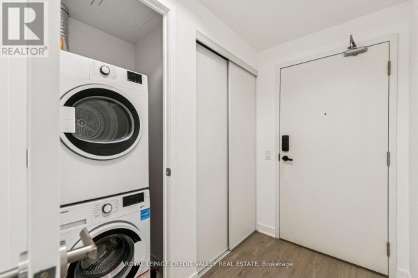 Laundry area in the entryway with stacked washer and dryer units. - 1413 - 3900 Confederation Parkway, Mississauga
