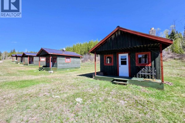 Row of small, green cabins with red trim and metal roofs on a grassy field. - 14167 Batnuni Lake Road, Quesnel