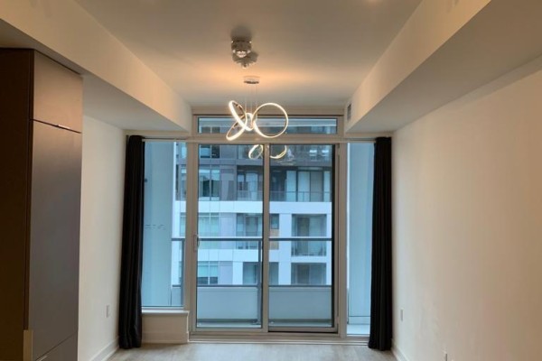 Living room with large sliding glass doors, dark curtains, and a modern circular light fixture. - 1416w - 27 Bathurst Street, Toronto