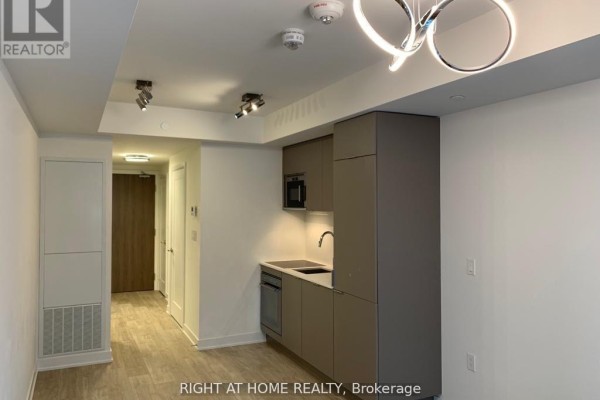 Studio apartment with a modern grey kitchen, integrated appliances, and a hallway leading to a door. - 1416w - 27 Bathurst Street, Toronto