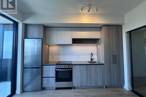 Compact kitchen with light wood cabinets, stainless steel appliances, and white tile backsplash. - 1418 - 181 Sterling Road, Toronto
