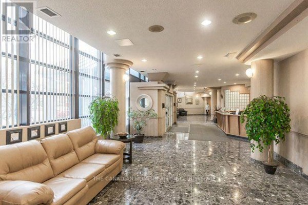Building lobby with marble floors, large windows, leather sofa, elevator entrance, and reception desk. - 1418 - 35 Trailwood Drive, Mississauga
