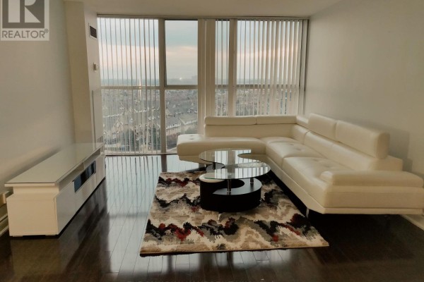 Living room with white sectional sofa, coffee tables, rug, entertainment unit, and city view. - 1418 - 35 Trailwood Drive, Mississauga