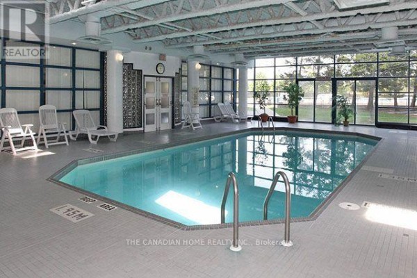 Indoor swimming pool with lounge chairs and large windows overlooking an outdoor green area. - 1418 - 35 Trailwood Drive, Mississauga