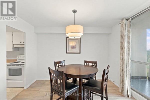 Dining area with light wood floors, a round wooden dining table with four chairs, and a view of the city from a large window. - 1419 - 1 Massey Square, Toronto