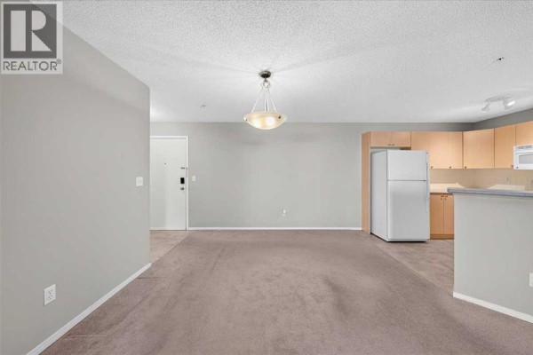 Living room and kitchen area with beige carpet, light grey walls, and light wood cabinets. - 142, 428 Chaparral Ravine View Se, Calgary