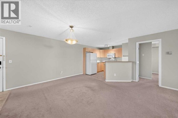 View of living room and kitchen area with beige carpet and grey walls. - 142, 428 Chaparral Ravine View Se, Calgary