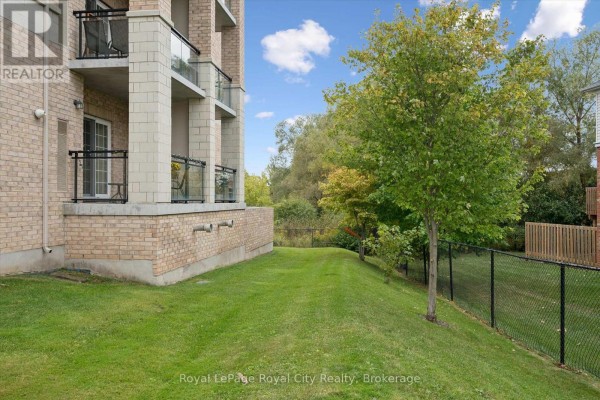 Side view of a brick apartment building showing balconies and a grassy area with trees. - 142 - 1077 Gordon Street, Guelph
