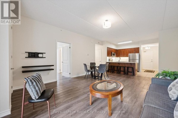 Open-concept living and dining area with a kitchen island, dark wood flooring, and modern furniture. - 142 - 1077 Gordon Street, Guelph
