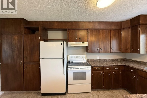 Kitchen with dark wood cabinets, white refrigerator, and white stove. - 142 2nd Street E, Glaslyn