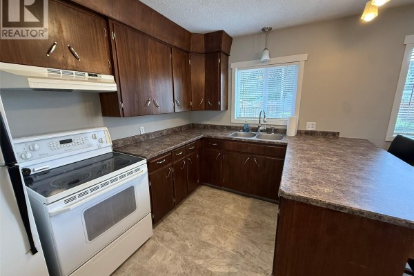 Kitchen with brown cabinets, countertop, sink, and window with blinds. - 142 2nd Street E, Glaslyn
