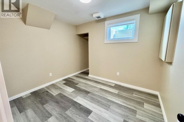 Empty bedroom with beige walls, grey plank flooring, and a window with horizontal blinds. - 142 Meadow Drive, Hinton