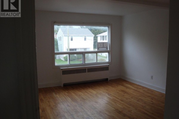 Living room with hardwood floors, white walls, and a large window showing houses. - 142 Ste Cecile Street, Ottawa