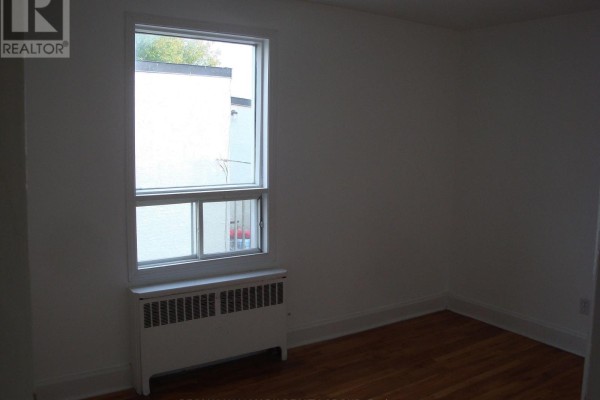 Small empty room with hardwood floors and a window with a view of a white wall. - 142 Ste Cecile Street, Ottawa