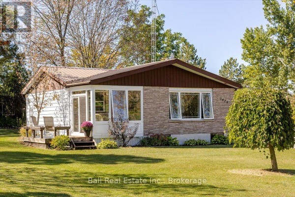 Front and side exterior of a bungalow with a lawn, mature trees, and a sunroom. - 1420 Eastview Drive, Selwyn