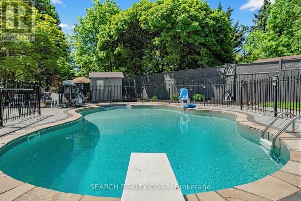 Backyard with a fenced oval swimming pool, diving board, and surrounded by a stone patio. - 1421 Watersedge Road, Mississauga