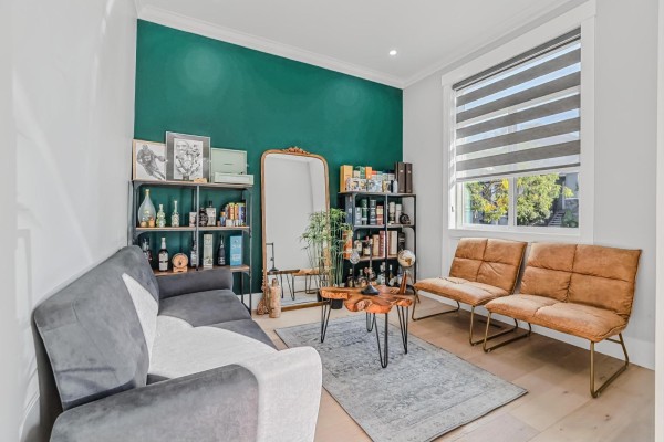 Living room with a dark green accent wall, grey sofa, two tan chairs, a mirrored vanity, and shelves. - 14215 61b Avenue, Surrey