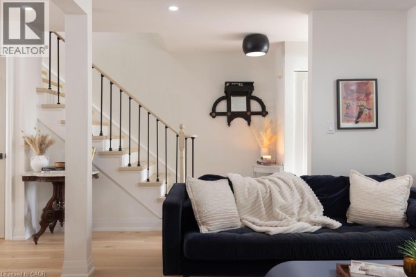 Living room with dark blue sofa, blanket, pillows, and staircase with black spindles. - 1422 Ghent Avenue, Burlington