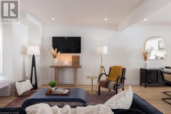 Living room with a sofa, armchair, television, and a doorway to the kitchen. - 1422 Ghent Avenue E, Burlington