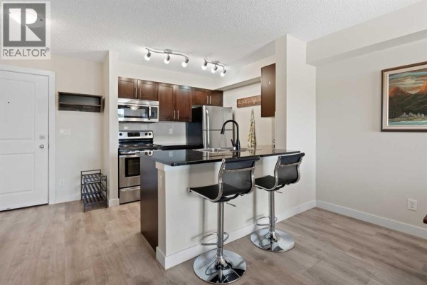 Kitchen and living area with dark wood cabinets and stainless steel appliances. - 1423, 81 Legacy Boulevard Se, Calgary