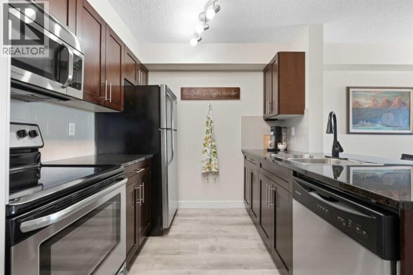 Kitchen with granite countertops, stainless steel appliances, and dark wood cabinets. - 1423, 81 Legacy Boulevard Se, Calgary