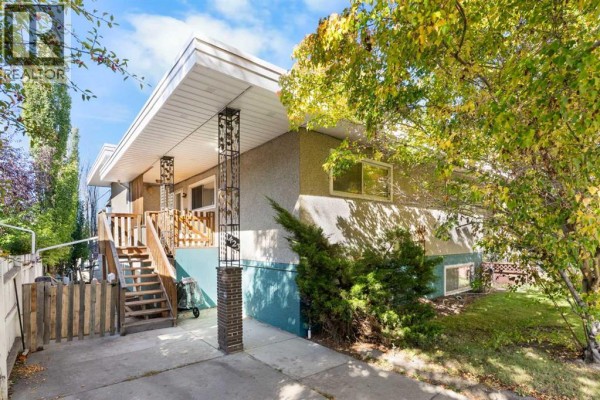 Front exterior of house with stucco and teal lower siding, mature trees with yellow autumn leaves. - 1423 16 Street Ne, Calgary
